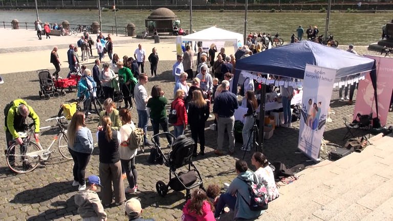 Mehrere Menschen nehmen am Deutschen Eck in Koblenz an einer Kundgebung am Welthebammentag teil