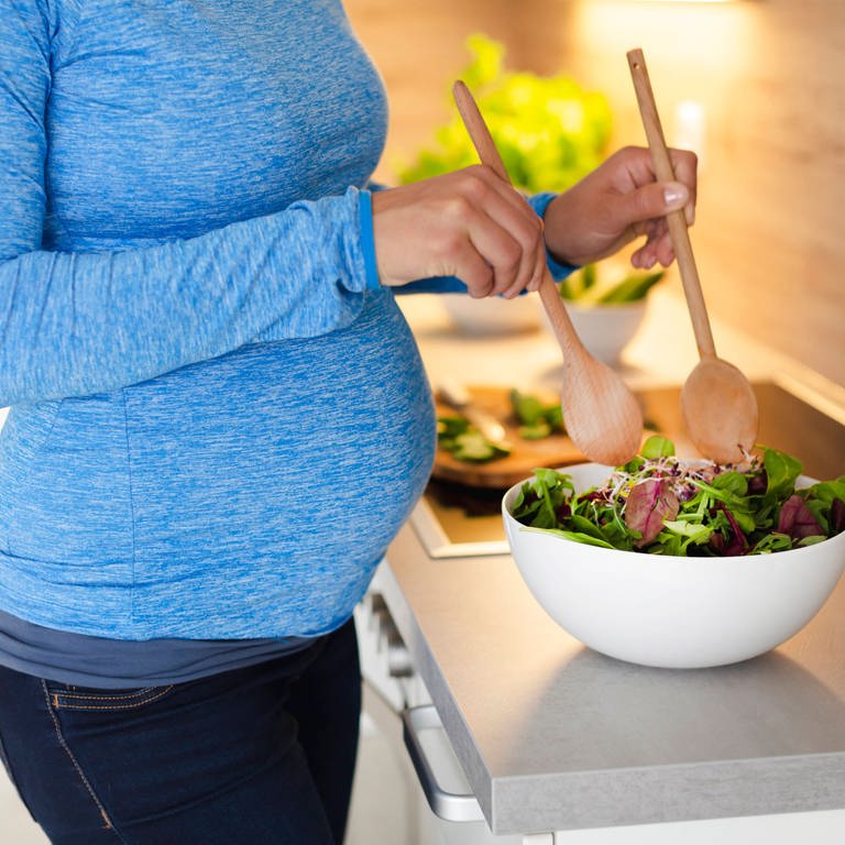 Eine Schwangere bereitet in der Küche einen Salat zu (Foto: IMAGO, IMAGO / Westend61)